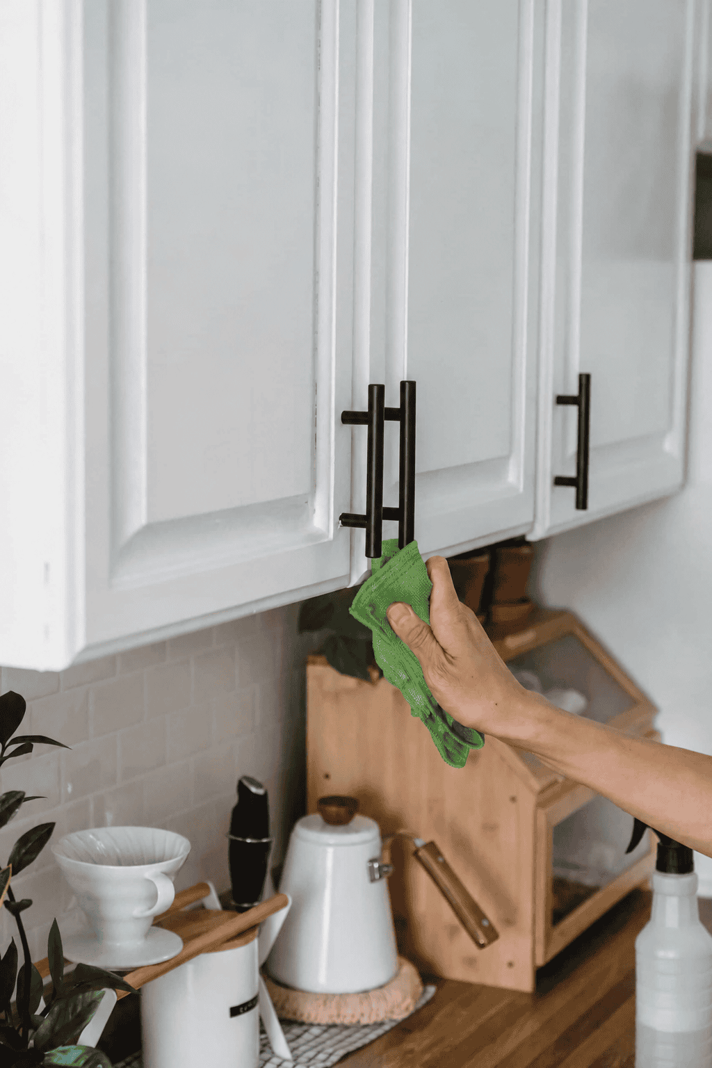 Hand wiping a black cabinet handle with a green microfiber cloth